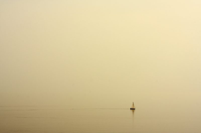 Ein kleines Segelboot am Horizont eines unüberschaubaren, nebligen Meers